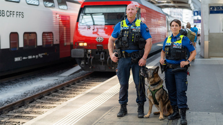 Zwei Sicherheitsbeamte der SBB auf dem perron und ein Zug fährt im Hintergrund ein.